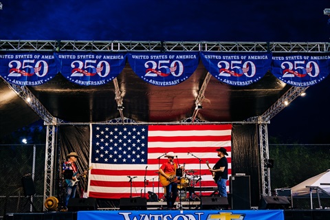 America 250 banners and American flag with stage and Mark Miller Band